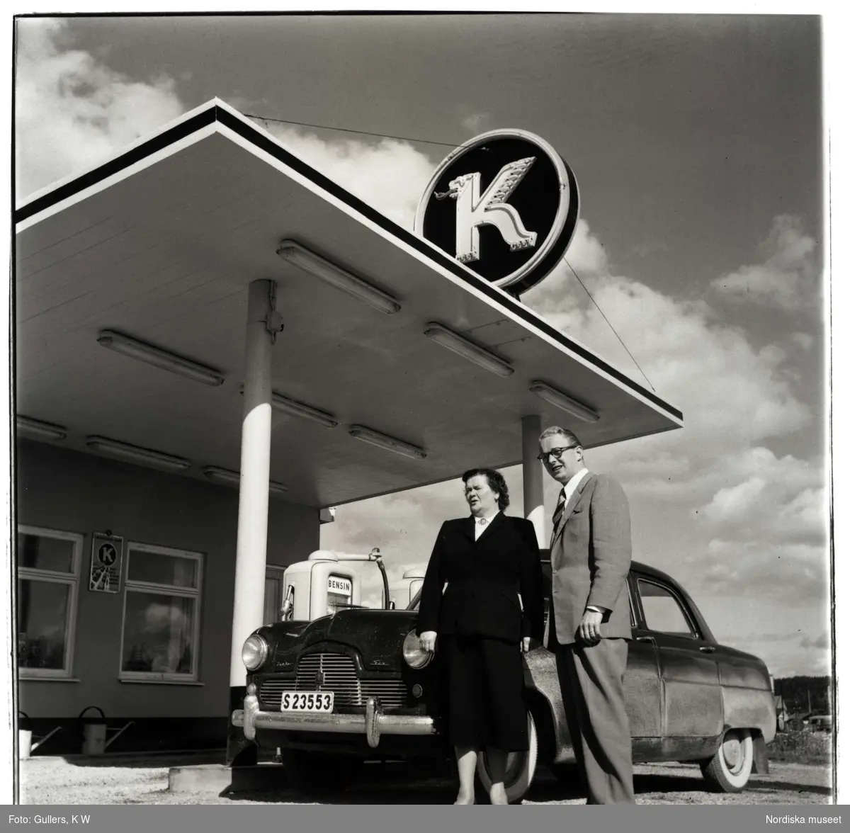 Koppartransmack, Karlstad. Par, man och kvinna, framför bil vid bensinstation.