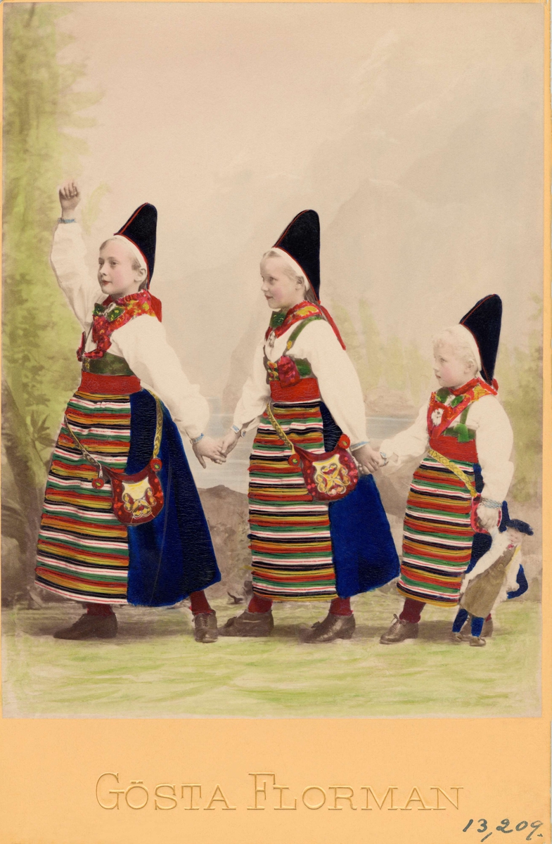 Tre flickor på rad, klädda i likadana folkdräkter. Olika åldrar
