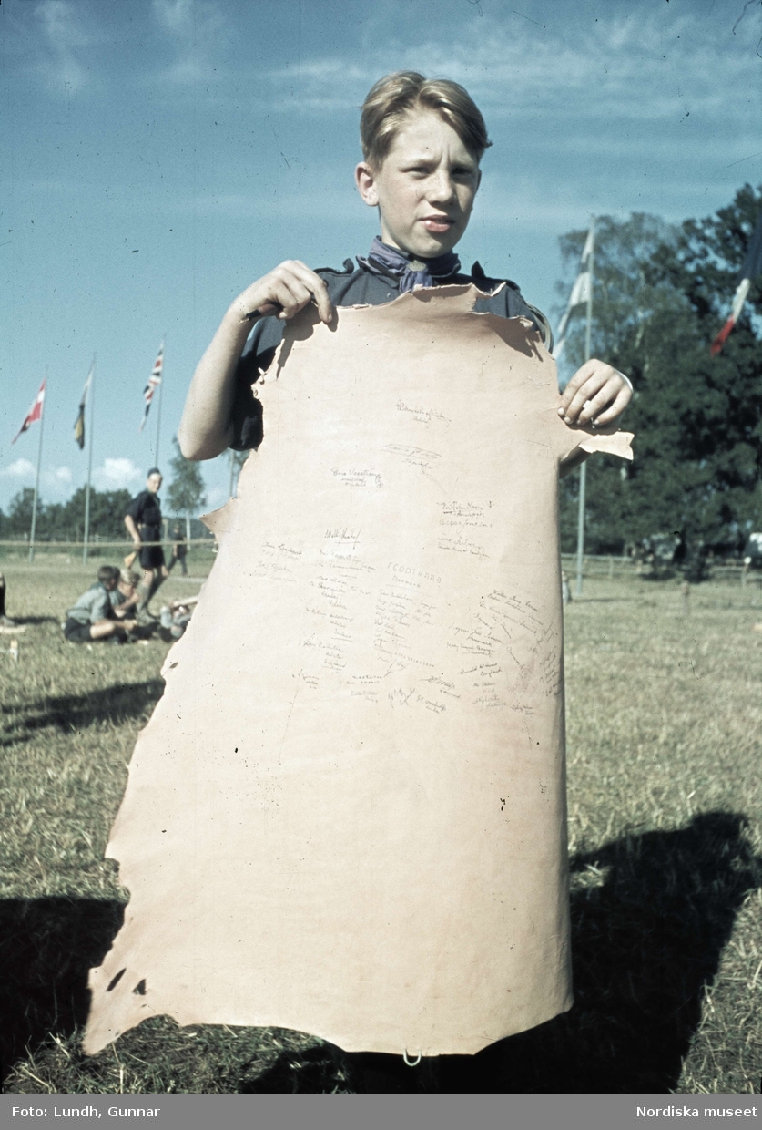 Scoutläger vid Tullgarn. En pojke håller upp ett skinn med namnteckningar.