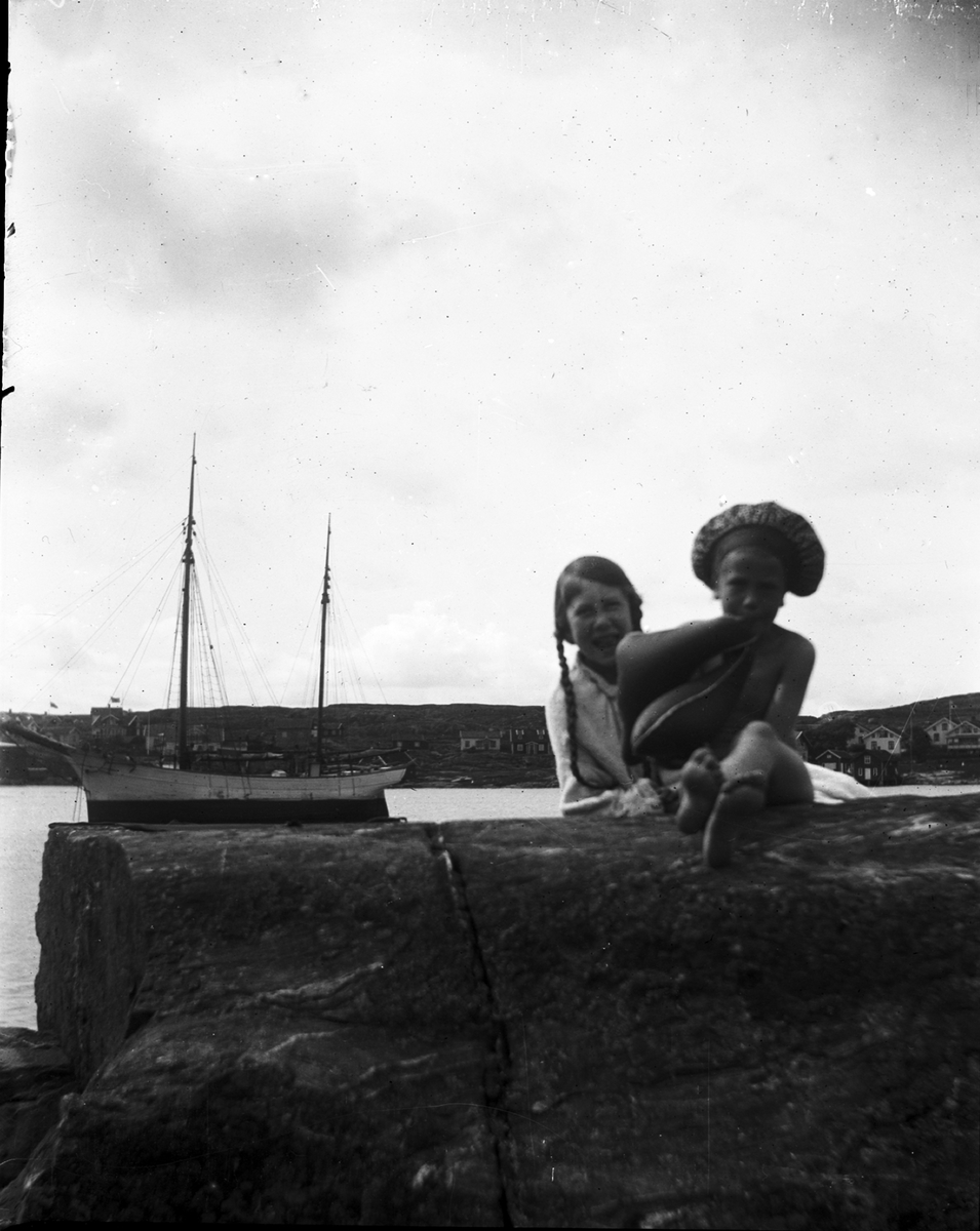 Två flickor på klipphäll, i bakgrunden segelbåt. Troligen i Fiskebäckskil, Bohuslän.