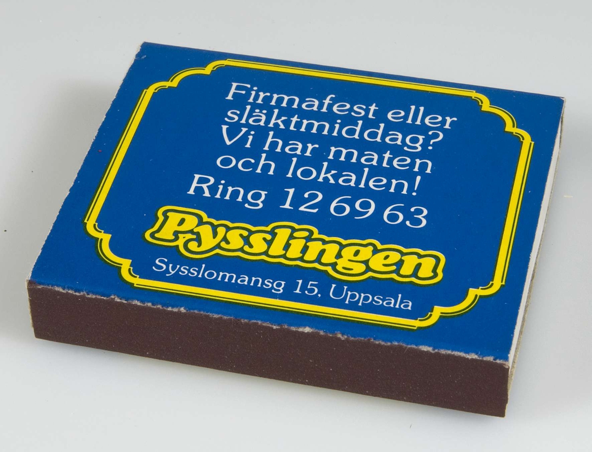 Blå och gul tändsticksask av papp med reklamtext för restaurang Pysslingen, Sysslomansgatan 15, Uppsala. Vitt svavel på tändstickorna.