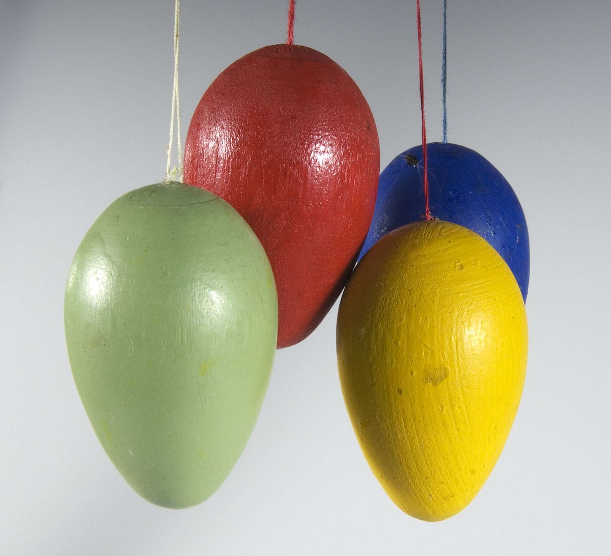 18 små ägg av trä målade i olika färger; gult, rött, blått och grönt med en liten trådögla för upphängning i påskris. Förvaras i pappask med påskrift: PÅSK.

