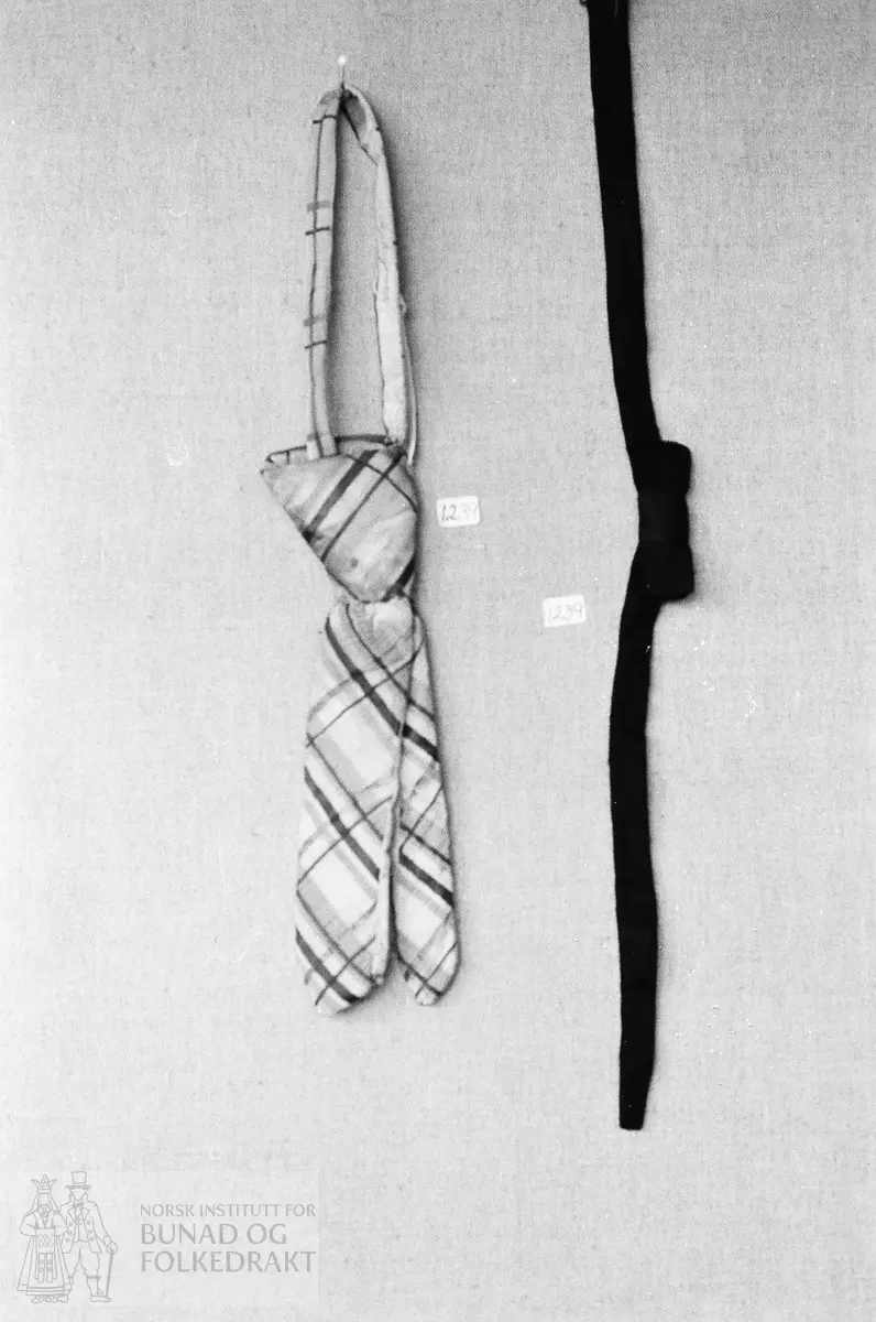 Sløyfe og slips. 

1: Ferdig knytt slips i hvit silkerips med rutemønster i blått, rødt og grått. Smalt band rundt halsen med stivespile i den ene enden til å stikke ned i knuten.

2: Svart silkesløyfe med svart smalt bånd og liten sprette.