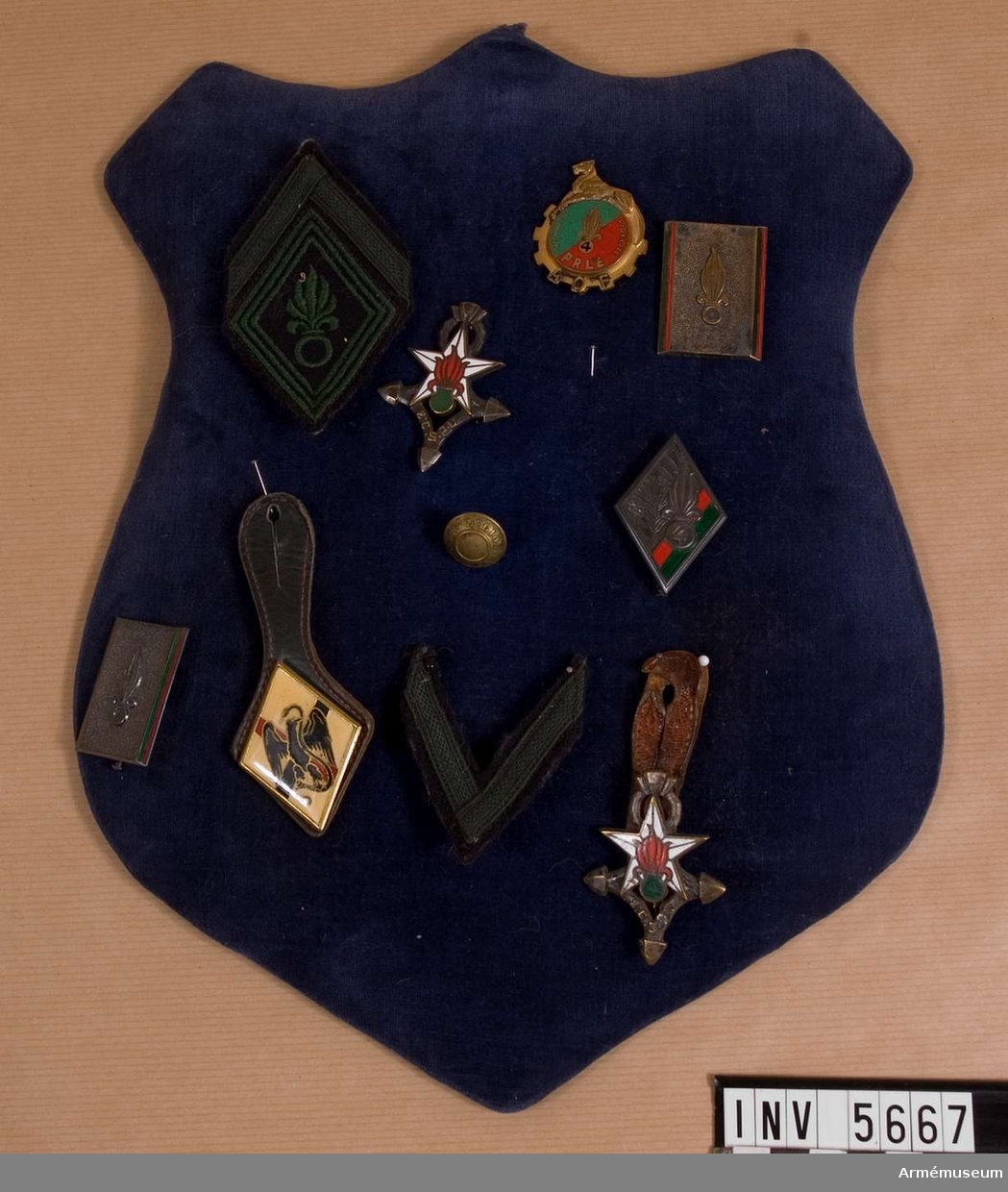 Märkessköld med regementsemblem från Franska främlingslegionen. Tio tecken placerade på en med mörkblå sammet överklädd sköld.