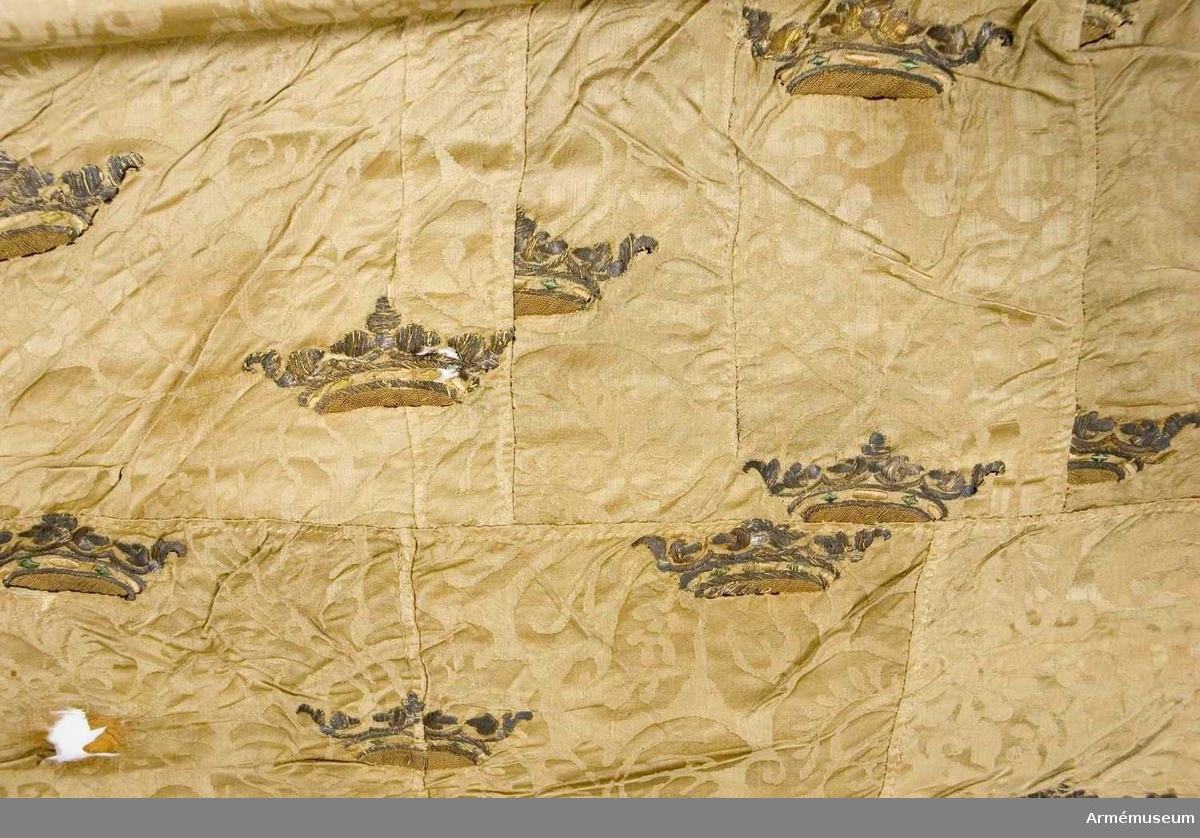 Fragment av en fana i vit sidendamast med broderade kronor. 
Duk: Tillverkad av enkel vit sidendamast. Damast från 1600-talets mitt.

Dekor: Broderad med strödda öppna guldkronor med stenar av grönt och svagt rosa silke, kronfodret gulaktigt. Duken i nedre delen fäst vid stången över linnetyg som ligger närmast stången. 

Stång: Tillverkad av furu. Nedanför dukens fäste lindat ett mönstervävt band i ca 470 mm fastsatt med tennlickor. 

Märkning på stången, inristat högst upp, strax nedanför dukens nedre kant: "K". Längre ner: "E.A.V.H" och "F.B.  ,   W". Längst ner inristat på stången sju stycken streck (IIIIIII).

Duken endast fragmentarisk. Damastens stadkant grön.