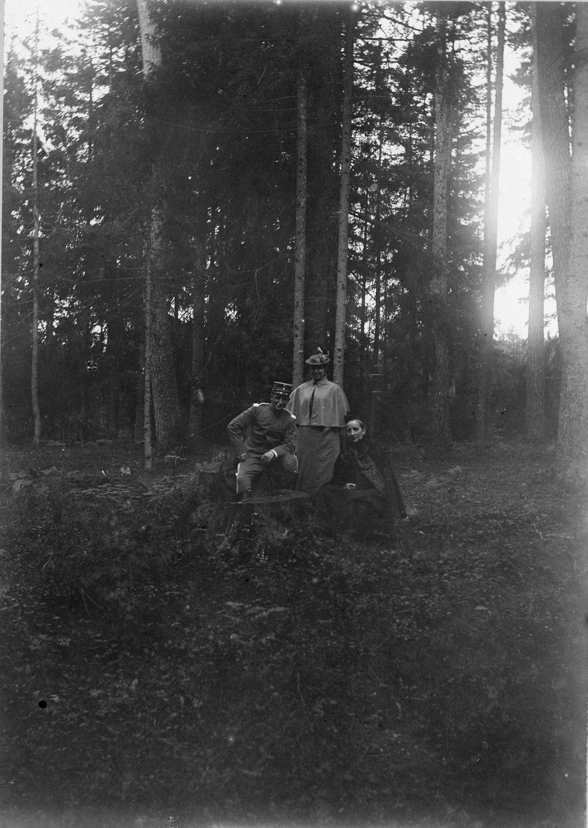 Soldat sittande på stubbe i skogen i sällskap med två kvinnor, Uppsala 1895.