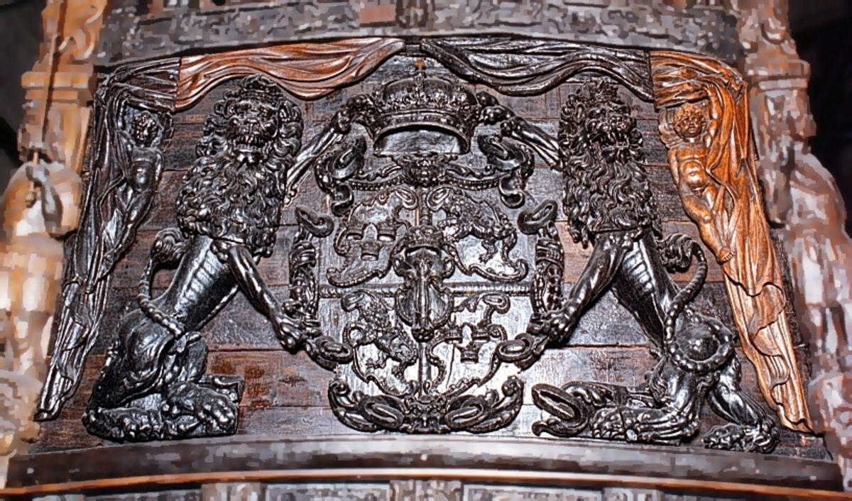 Skulpterad sköld, med upprätt, mot höger gående lejon. Lejonet är snidat i hög relief, med en heraldiskt stiliserad hållning. Sköldens kontur är rokokomässig, med kanter av varierande bredd och rik pärlbroskdekoration. Den vänstra kanten är något insvängd på mitten. Upptill avslutas skölden med en ellipsformad broskvolut. Baksidan är slät.

Text in English: Shield with upright, rightward-facing lion. The lion is carved in high relief and reproduced in perspective. It is seen in profile, and its posture is heraldically stylised. The shield has an almost rococo-like outline, with edges of varying width and rich earshell work decorations. The left-hand edge of the shield is somewhat narrowed at the middle.The top the shield is finished with an ellipse-shaped pearlwork scroll. The reverse side is smooth.