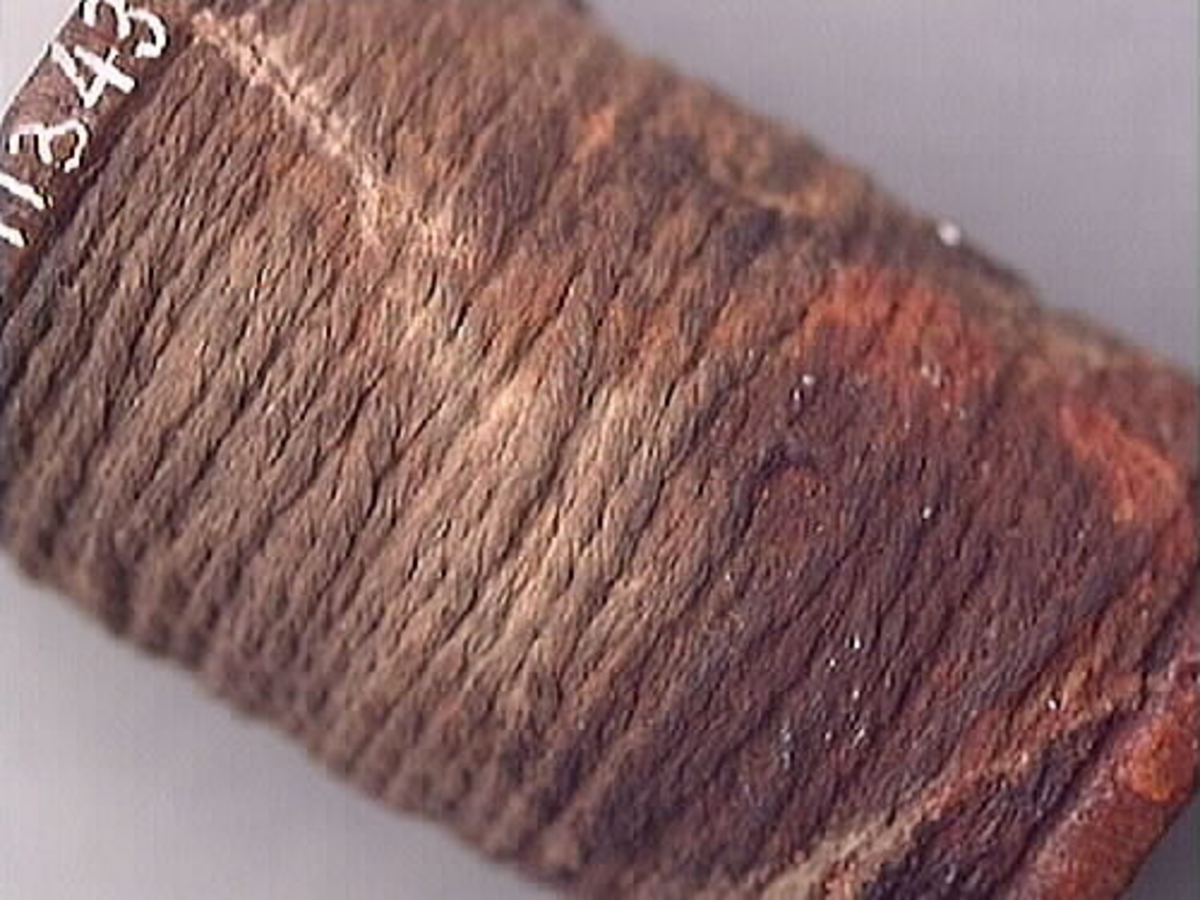 Trärulle med upplindad rev eller snöre. Rullen är rödaktig i färgen. Snöret har rostliknande fläckar. Trärullen och reven är välbevarad.