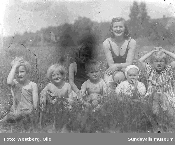 Kvinna med sex barn sittandes i gräset.