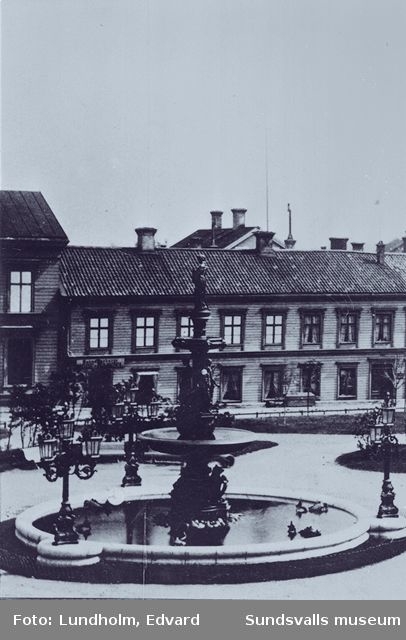 Bilden visar i förgrunden Gisbergs fontän vid Vängåvan, i bakgrunden "kopparslagare Modins hus" i kvarteret Proserpina.
