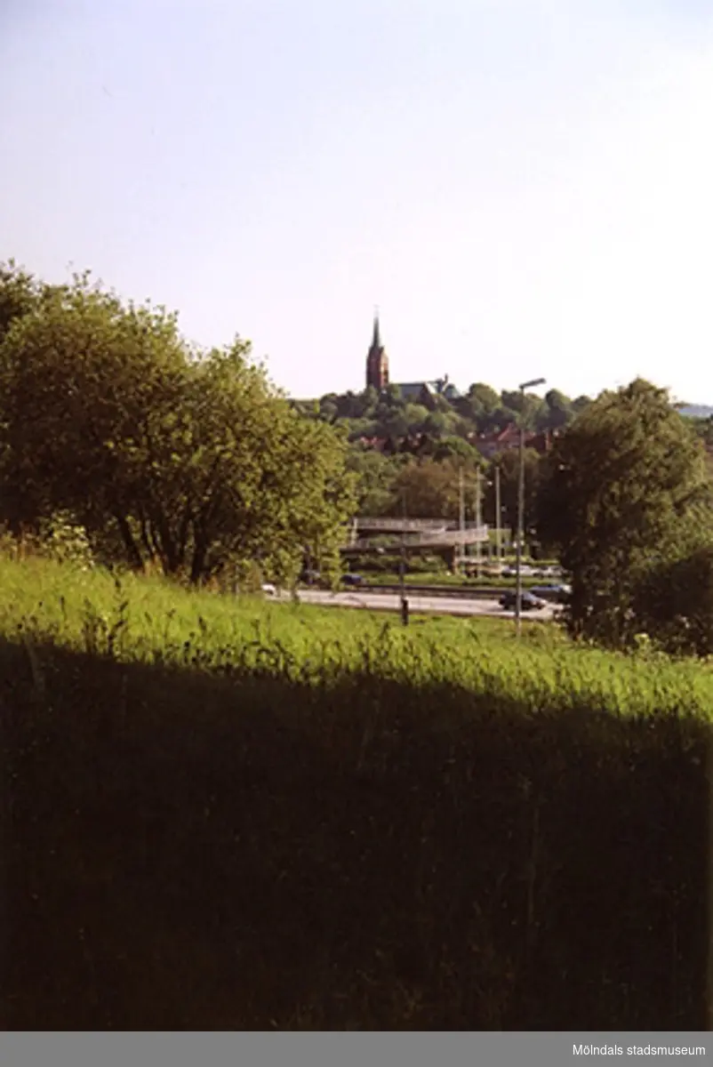Utsikt över ängen mot Fässberg kyrka i bakgrunden. Järnvägsgatan i bildens mitt.