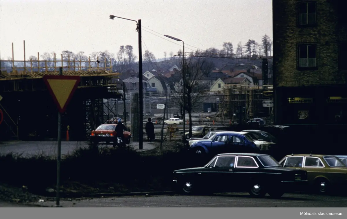 Mölndals Bro under uppförande, år 1975. Bilar står parkerade på Broplatsen. I bakgrunden ses bebyggelse i Broslättsområdet.
