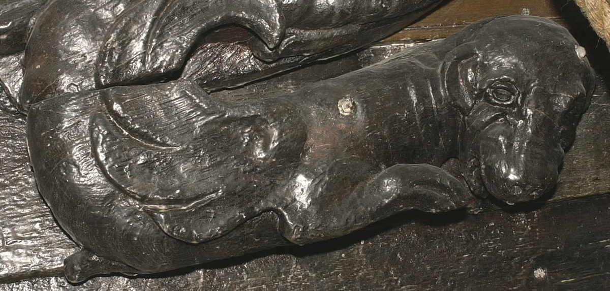 Skulptur av en säl, hund eller drake, återgiven i höger profil med det nedböjda huvudet riktat åt sidan.
Sälen har ett stort, trekantigt huvud med stora ögon och hängande öron. Foten är fenliknande. Den drakliknande stjärten fortsätter uppåt och avtecknar sig längs med stjärten till en triton, se fyndnummer 23079. Baksidan är slät.
Skulpturen är mycket välbevarad.

Text in English: A sculpture of a seal, dog or dragon carved in right profile with its bowed head turned to the side.
It has a large triangle shaped head with large eyes and hanging ears. Fin-like tail end. The dragon-like tail extends upwards onto a Triton situated above, see No. 23079.  The back is smooth.
The sculpture is very well preserved.