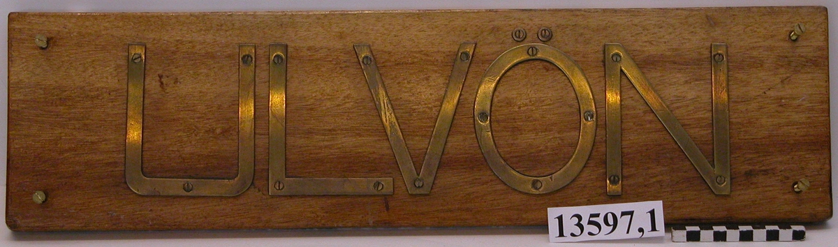 Bokstäverna av mässing bildande namnet"Ulvön" fastsatta med skruvar på en träplatta.
Neg,nr 5925.