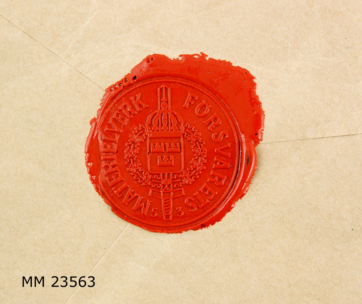 Två stycken runda sigillavtryck i rött lack på baksidan av brunt kuvert. I mitten av sigillet , krönt sköld med tre kronor liggande på ett svärd samt omgivet av serafimerkedja. Längs kanten text: " FÖRSVARETS MATERIELVERK " I det ena avtrycket står siffrorna " 53 " i det andra, siffrorna " 39 ". På kuvertets framsida tryckt text: " Assureras för Ettusen ( 1000 ) kronor. ( Texten är understruken ) . Tjänste, Krigsmakten, Försvarets Bok- och blankettförråd, 172 20 SUNDBYBERG. Liten röd rektangulär påklistrad lapp med text: " V  Sundbyberg 1 Nr 740 " Adresserat till: " Marinmuséet och modellkammaren, 371 00 KARLSKRONA. Dessutom skrivet med blå kulspetspenna: " 530, 5, 35 "