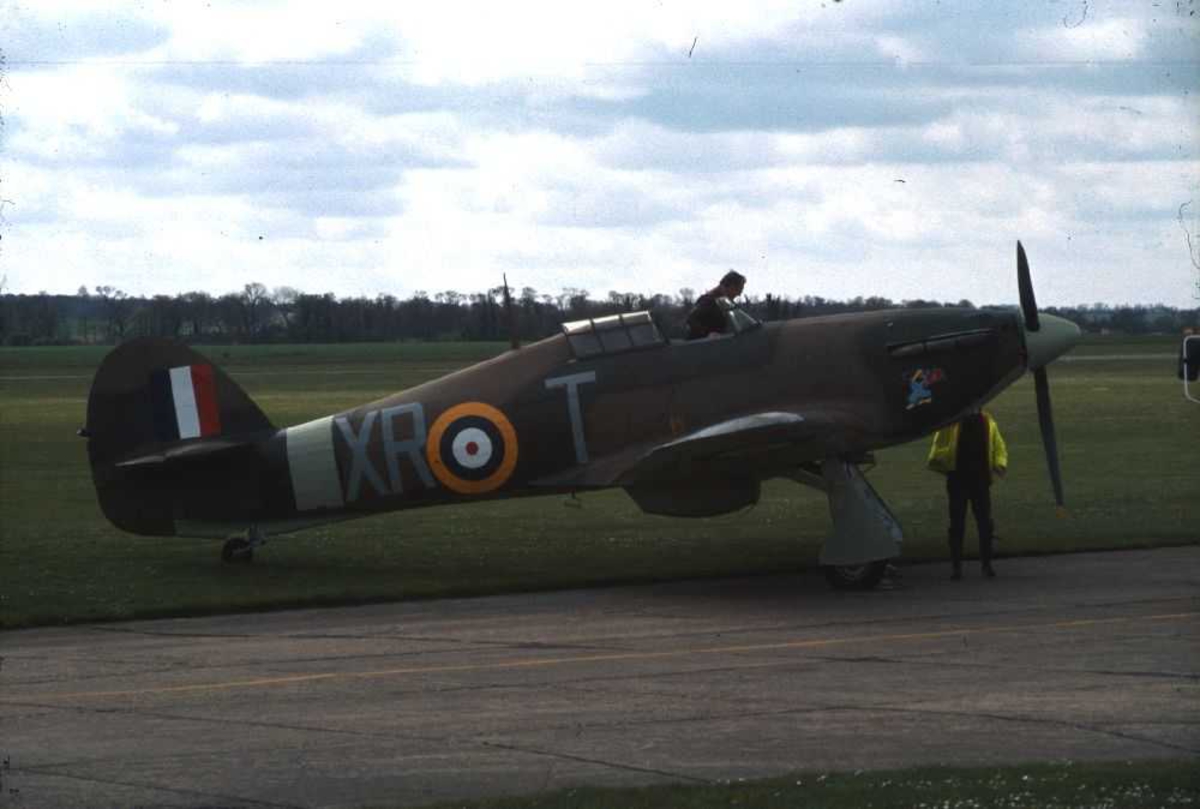Ett fly på bakken, Hawker Hurricane Mk12A, X-RT. En person i cockpiten og en person ved flyet.