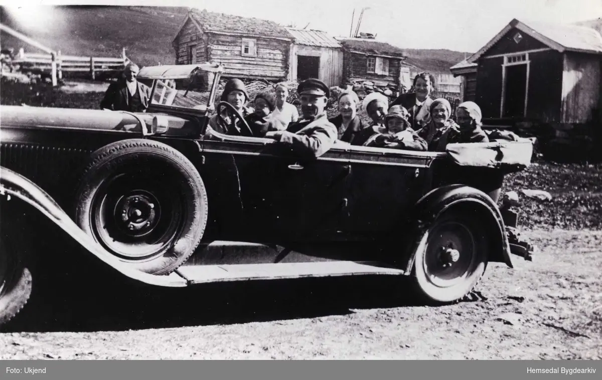 Biletet er teke på Storejorde, 53/7 i Lykkja. Bilen er ein Nasch 1927-modell, og den fyrste personbilen som Hemsedal Bilselskap kjøpte. Sjåføren er Ole H. Løken. Med i bilen er kona og dei to borna, og elles slektningar og vener. Litt av ein sundagstur i 1932.