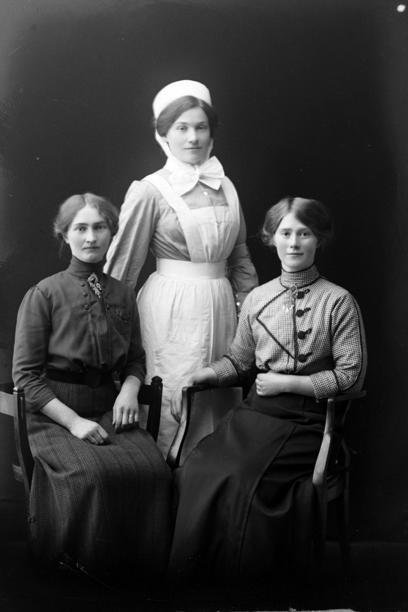 Studioportrett av tre unge kvinner. Én av dem har sykepleieruniform.