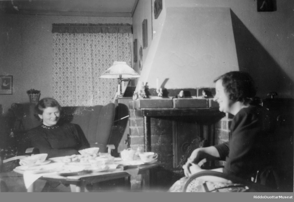Guokte rivgu cohkkaba biise guorras ja juhkaba gáfe.
To damer sitte inne ved peisen å drikker kaffe.