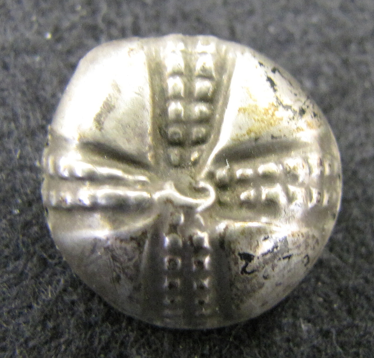 Mindre knapp med ögla av silver, korsformigt ornerad på översidan. Från trakten av gamla Lödöse.