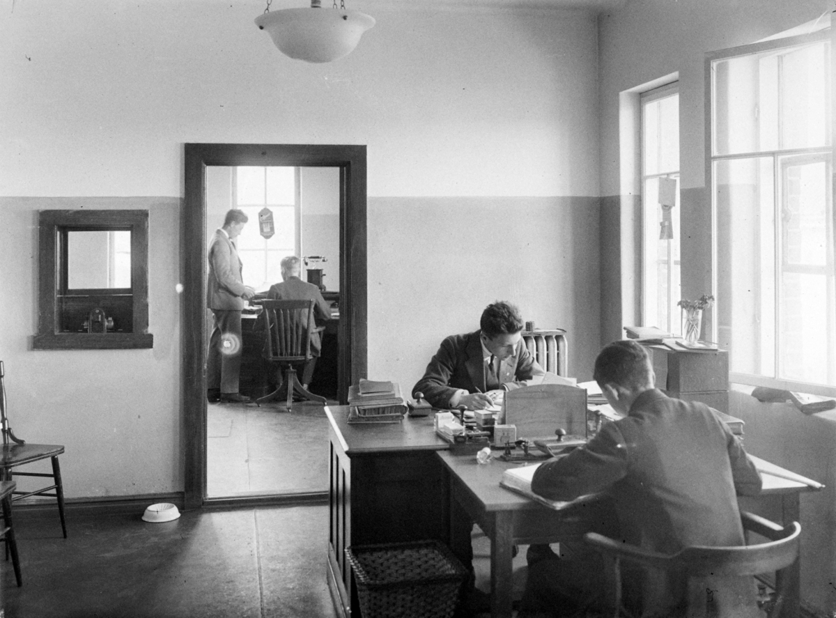 Interiørbilde fra kontoret i FM Teglverkskontor, med unge menn i arbeid ved skrivebordene.