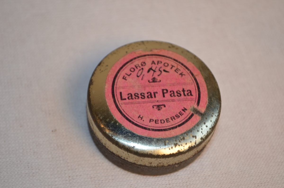 Rundt liten bok for Lassar Pasta (sinksalve). Det er framleis salve igjen i boksen. Rosa logo på topp som viser at produktet kjem frå Florø Apotek og har koste 0,45 kroner. Låg i veske KSF.011261.