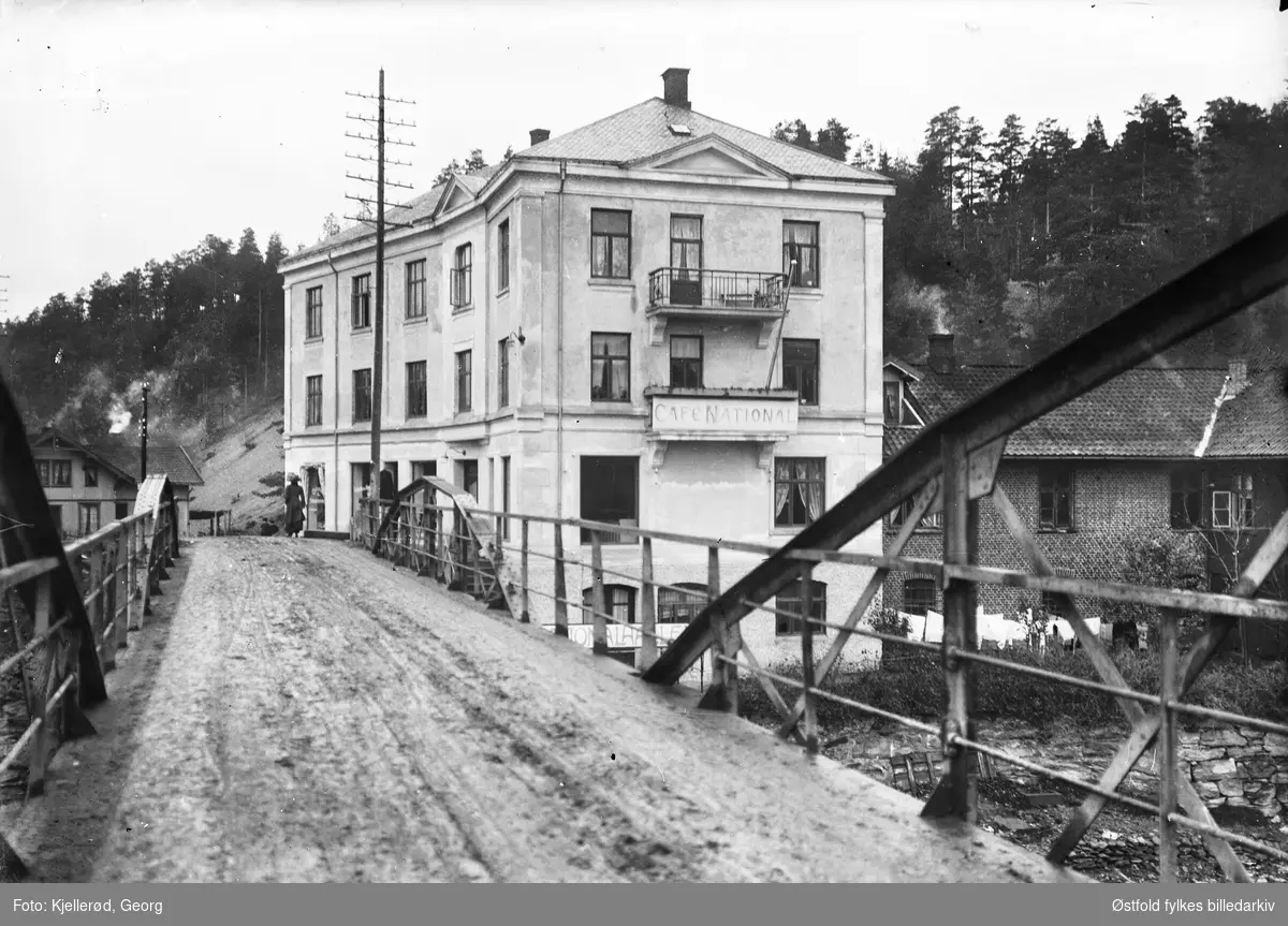 Notodden 1910, Gamle hovedvei, krysset Heddalsvei Tinnesgata, bygget brant for noen år siden og eksisterer ikke lenger. Vi står på brua over Tinnåa.
Cafe National.