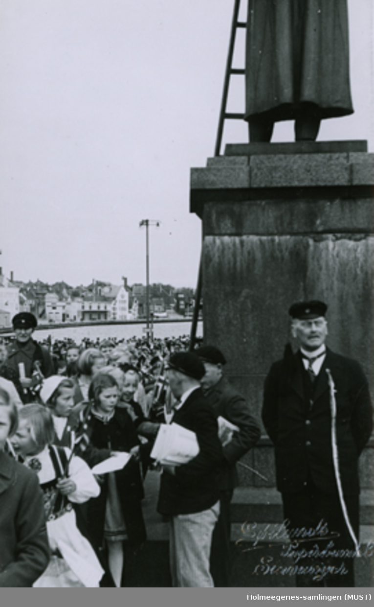 Festkledte mennesker ved sokkelen av en statue. 17.mai-feiring på torget i Stavanger.