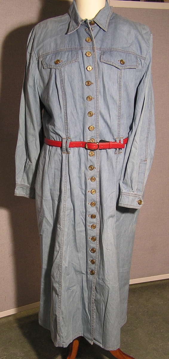 Lang kjole med lang erme, krave, og legg som minner om en arbeidsskjorte. Innsvinget i livet med stropper til belte. Skulder puter. Belte med. Stikklommer i sidenene og 2 klaffer som dekor på forstykket. Knappelukking foran. Splitt i siden på skjørtet.