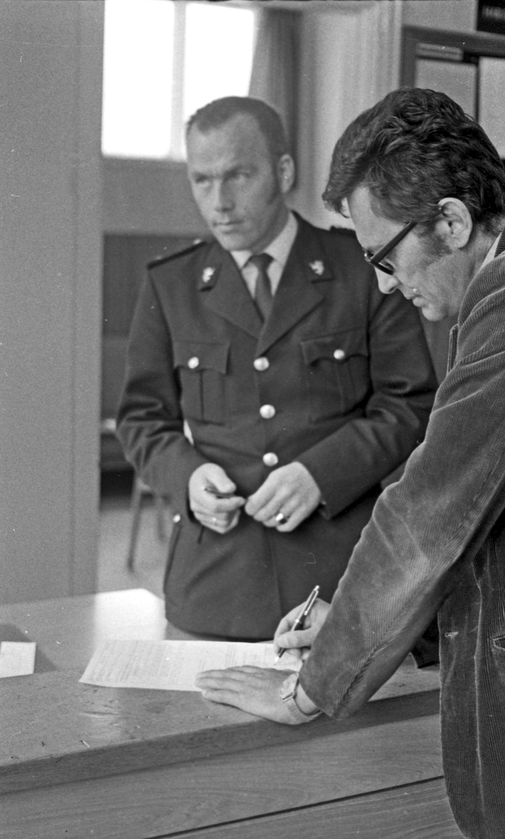 På politikammeret. Eldre politimann bak arbeidspulten. Foto fra resepsjonen - uderskriving av papirer.