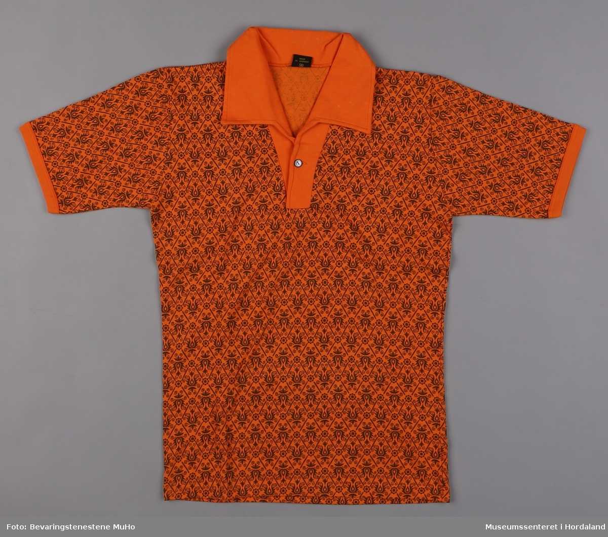 Oransje tennisskjorte med krage og knapping i halsen. Påtrykt stoff med blomsterdekor i brunt.