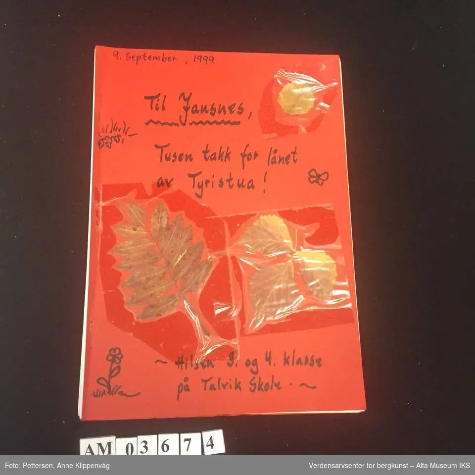 Et sitiftet hefte med rød forside og bakside. Pålimte tørkede løvblader. Inneholder ulike dikt, hilsener og tegninger laget av 3. og 4. klasse ved Talvik Skole i 1999, som takk for lånet av hytta.