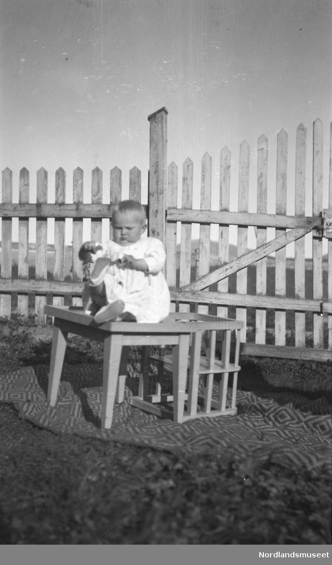 fra Velfjord, Unni Strand, som sitter på en barnestol. Et Et gjerde går i bakgrunnen.  Unni Strand, f. 1917, datter til lensmann A. Anderssen-Strand og Augusta f. Coll.