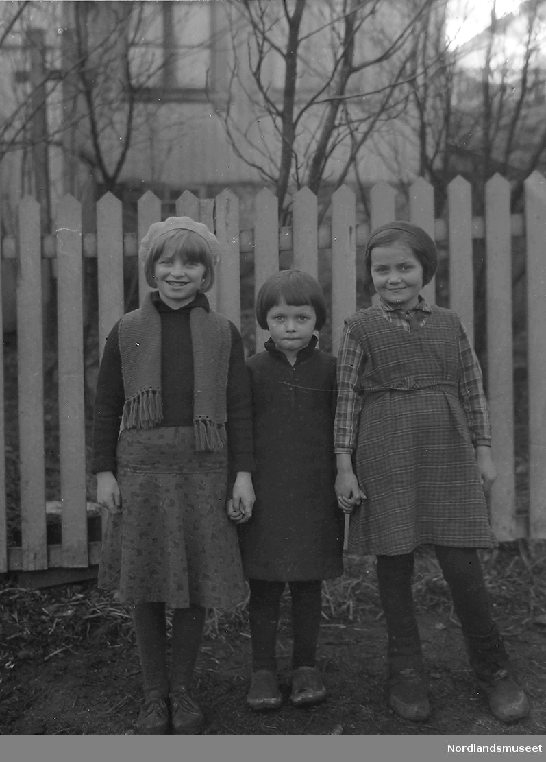 Tre jenter foran et stakittgjerde. 