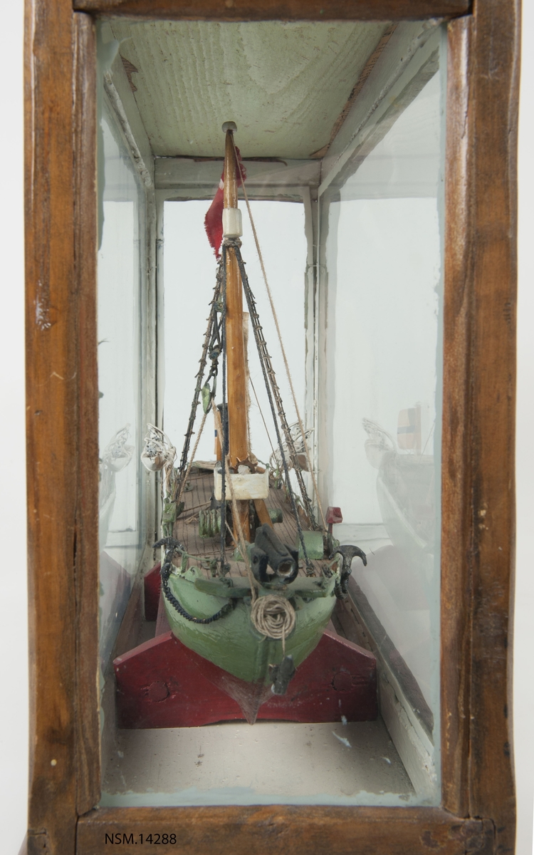 Enkel helmodell (sjømannsmodell) av hvalbåt i monter. Grønt skrog, mast, skorstein, 2 lettbåter, hvalkanon.