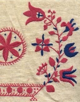 Broderat hängkläde på linnetyg med bomullsgarn i rosa och blått. Hängklädet har en 200 mm iknuten bred frans i lingarn i färgerna rött, blått och vitt.Fem olika motiv spridda över längden. Förlagan kommer från Stamnared och är från år 1845. Föremålet har en gammal märkning.