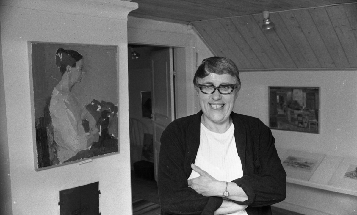 Inga Berg 5 april 1968

Provinskonstnär Inga Berg står i ett rum med träpanel på väggen och taket. I rummet finns också en kakelugn där det hänger en tavla på en kvinna.