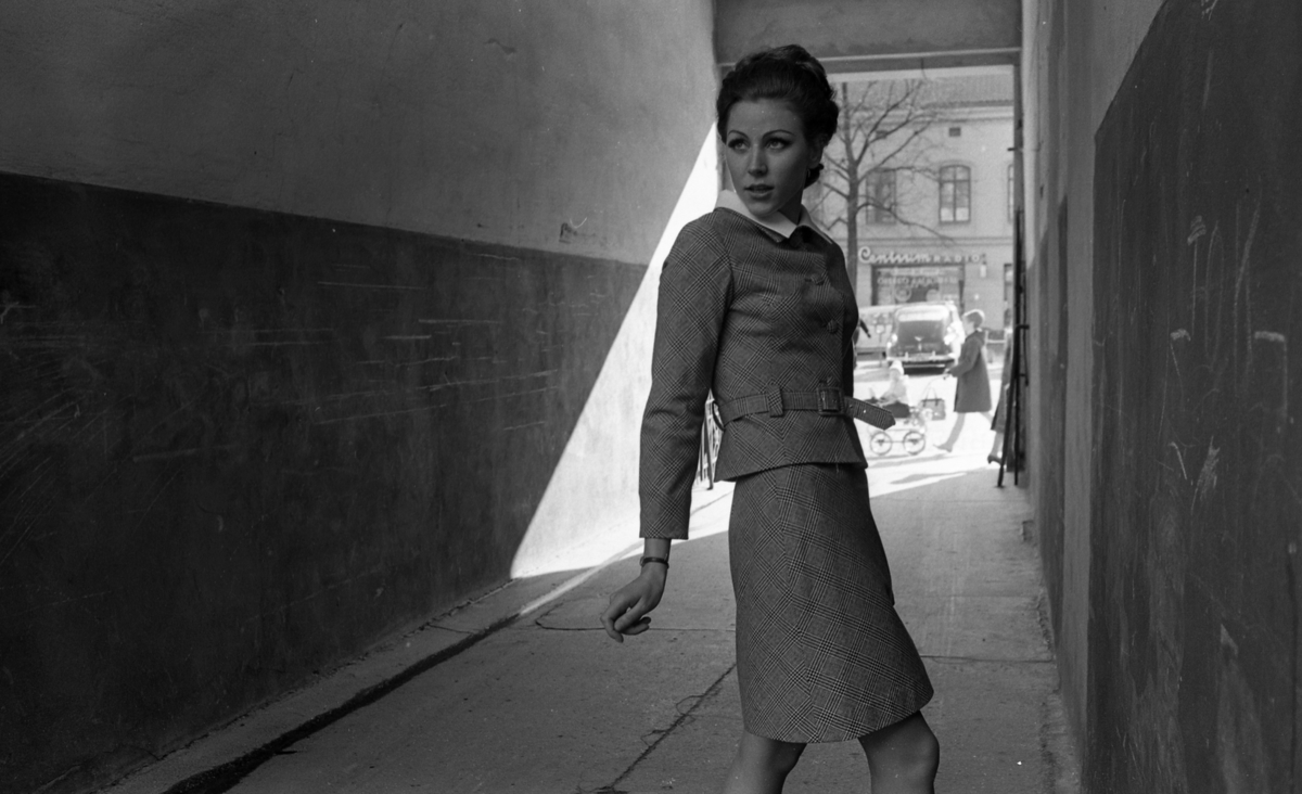 Modenummer Sand 30 april 1968

Mannekäng i dräkt med vit krage står i en portingång.
Bakom henne ser man Stortorget där bilar står parkerade, och en kvinna med barnvagn.