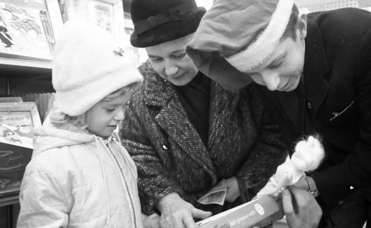 Julköprush, 7 december 1965

En ung man i tomteluva och svart kostym visar en docka och en förpackning för en liten flicka och en äldre dam.
