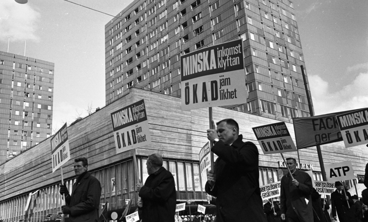 Första maj demonstration 2 maj 1967

Ett första-majtåg går genom centrala Örebro vid varuhuset Krämaren. I förgrunden syns tre män klädda i rockar och som bär på varsin demonstrationsskylt med texten: "Minska inkomstklyftan, ökad jämlikhet." Publik syns i bakgrunden.