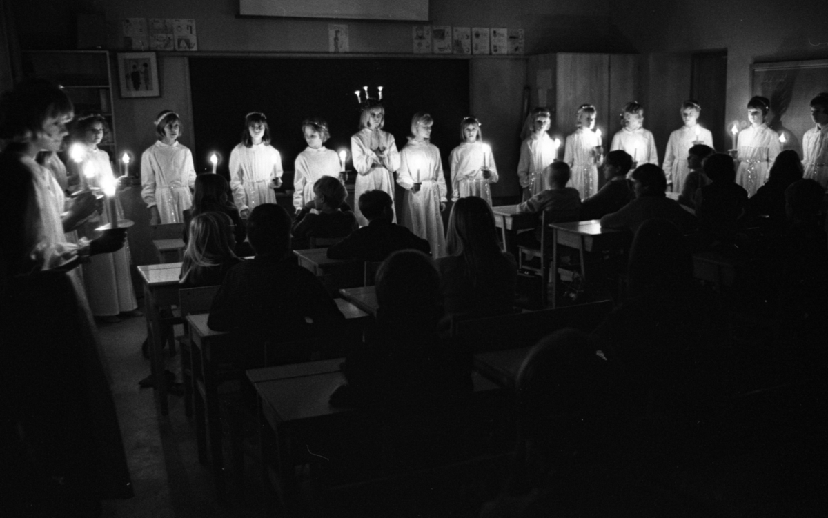 Luciafirandet 13 december 1966

En Lucia tärnor som är i tonåren står inomhus i ett klassrum i en skola. De är klädda i Lucialinnen. Lucian har Luciakrona på huvudet med ljus i samt ett rött skärp om livet. Hon håller ihop sina händer. Tärnorna bär glitterkransar i håret, glitterband runt liven samt bär ljus i sina händer. Lamporna i klassrummet är släckta. Publiken i form av en skolklass sitter stilla i sina skolbänkar och betraktar Luciatåget som står uppställda framför dem samt vid sidorna av klassrummet.