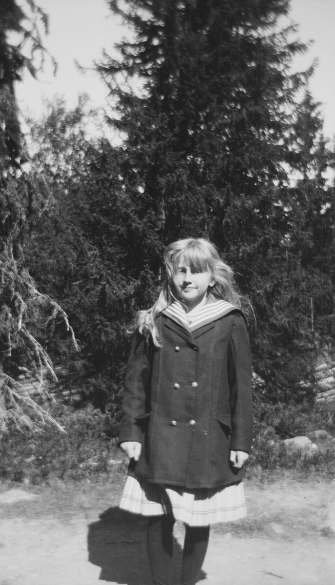En jente med flagrende hår står på en skogsvei.