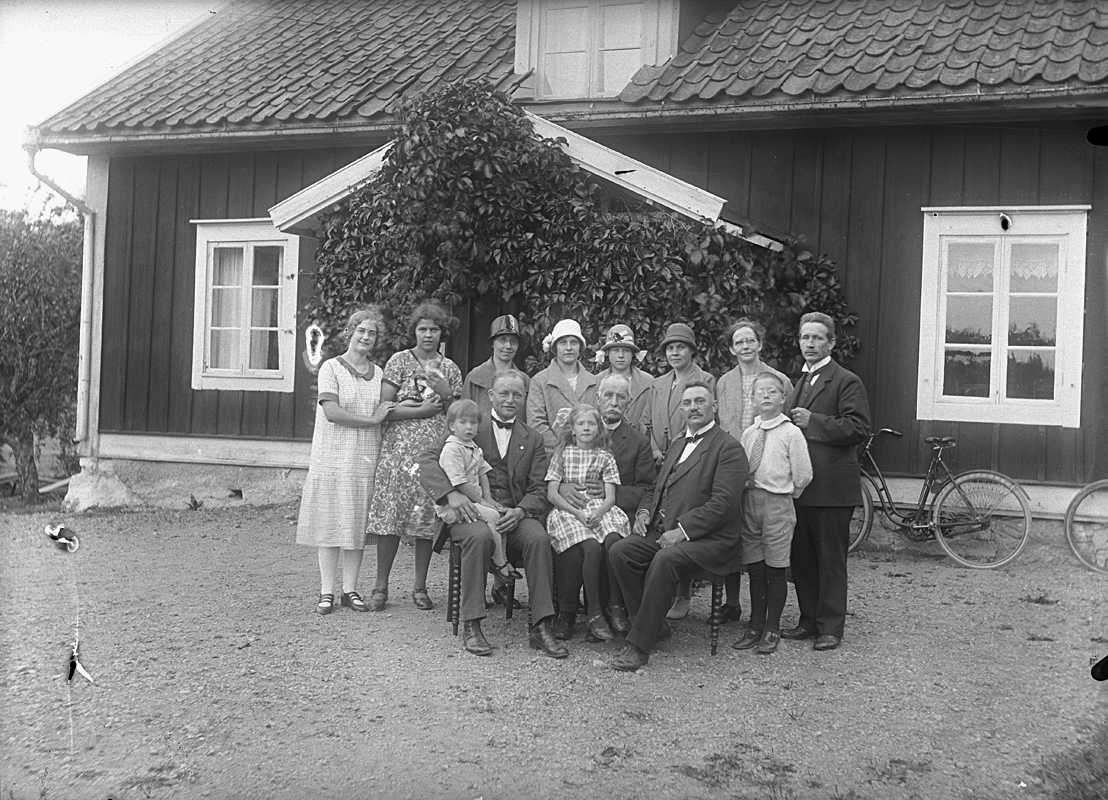 Bostadshus, grupp 14 personer framför huset.
Längst till höger Edit och Johannes Natanael Bäckman, och längst till vänster deras dotter Nanna Bäckman.
Nr. 3 från vänster Karin Berger (Höglund).