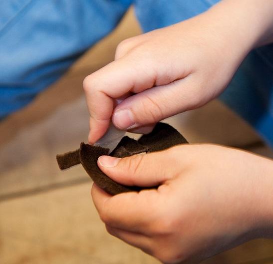 Nærbilde av barnehender som skjærer i en skinnbit med en steinflekke