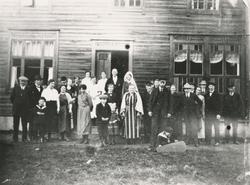 Gruppeportrett av brudefølget foran et hus med brudeparet An