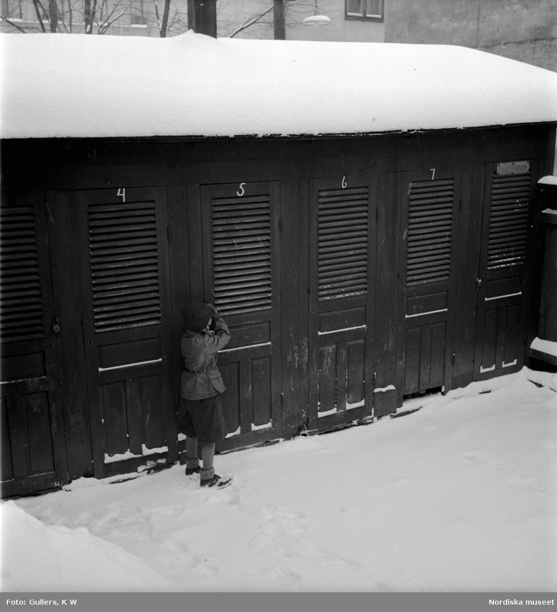Ett barn står utanför en rad med utedass tillhörande bostäder på Södermalm, Stockholm.