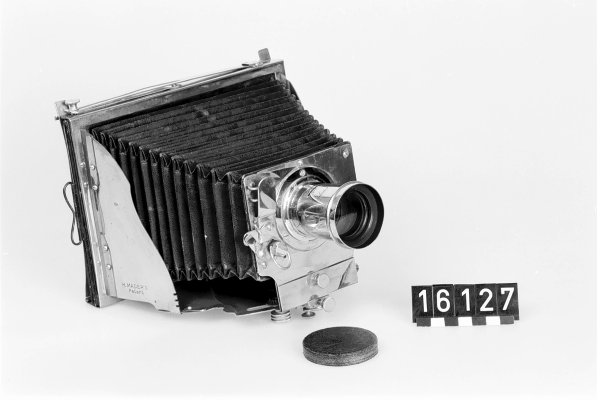 The first foldable metal camera, Model II. Constructed with a patent by H. Mader from 1888-1890. The camera was donated to the museum in January 1939.
The camera is marked with a "5" on the bellows' folds and with a circular mark bearing the letters G M R and two sword-like symbols.
The lens is marked "Aplanal Invincible" and has "VI" engraved on the back near the threads. The camera comes with 4 cassettes, 5 insert apertures, and a fabric-covered case.