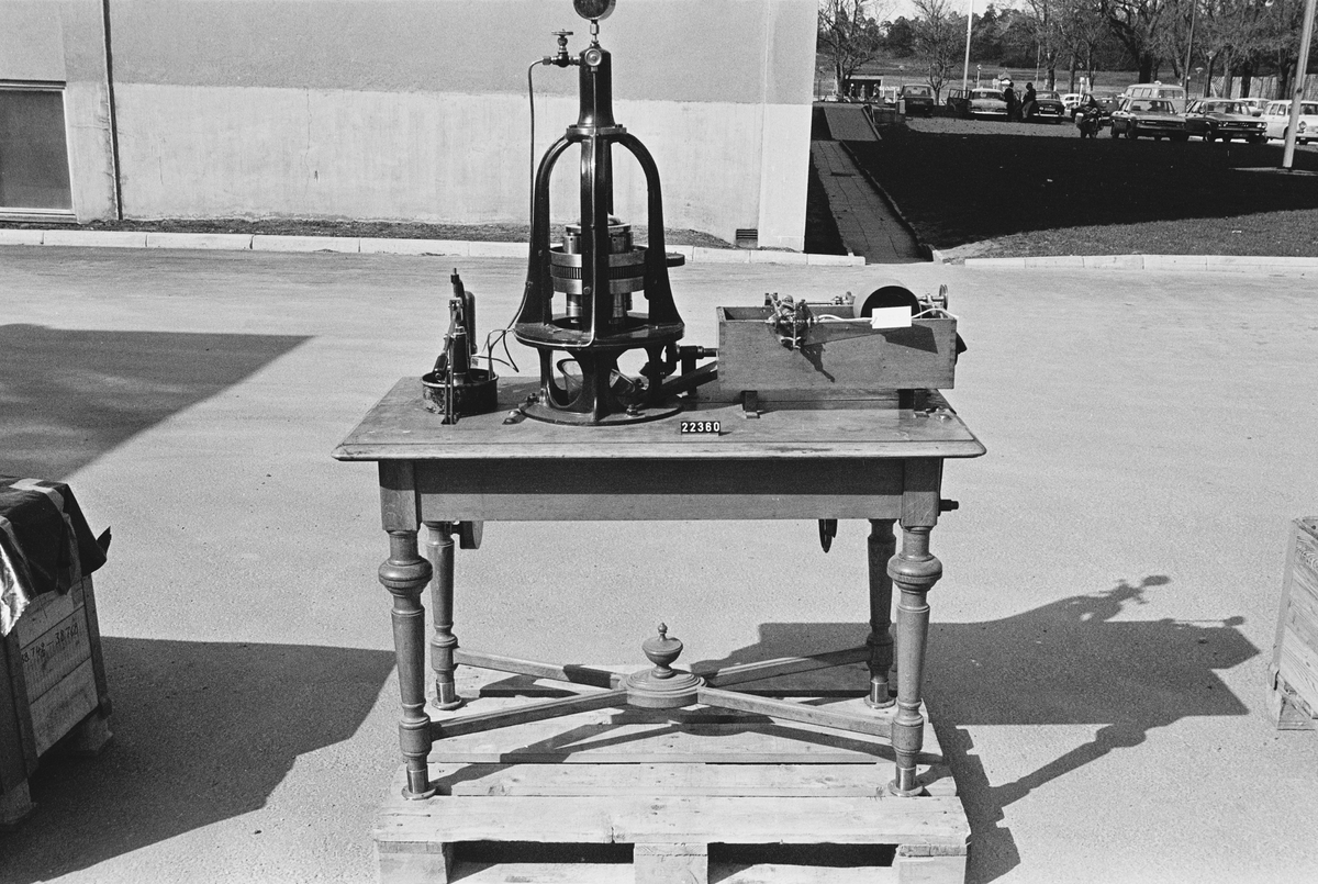 Maskin för pressning och spinning av garn av nitrocellulosa, konstruerad av R.W. Strehlenert. Monterad på ett bord med låda. Med maskinen följde en härva silkegarn, troligen spunnet på maskinen.  Utställningsskylt om föremålet: "Maskin för pressning och spinning av garn av nitrocellulosa, konstruerad av R.W Strehlenert och tillverkad i Paris. Tekniska museet"