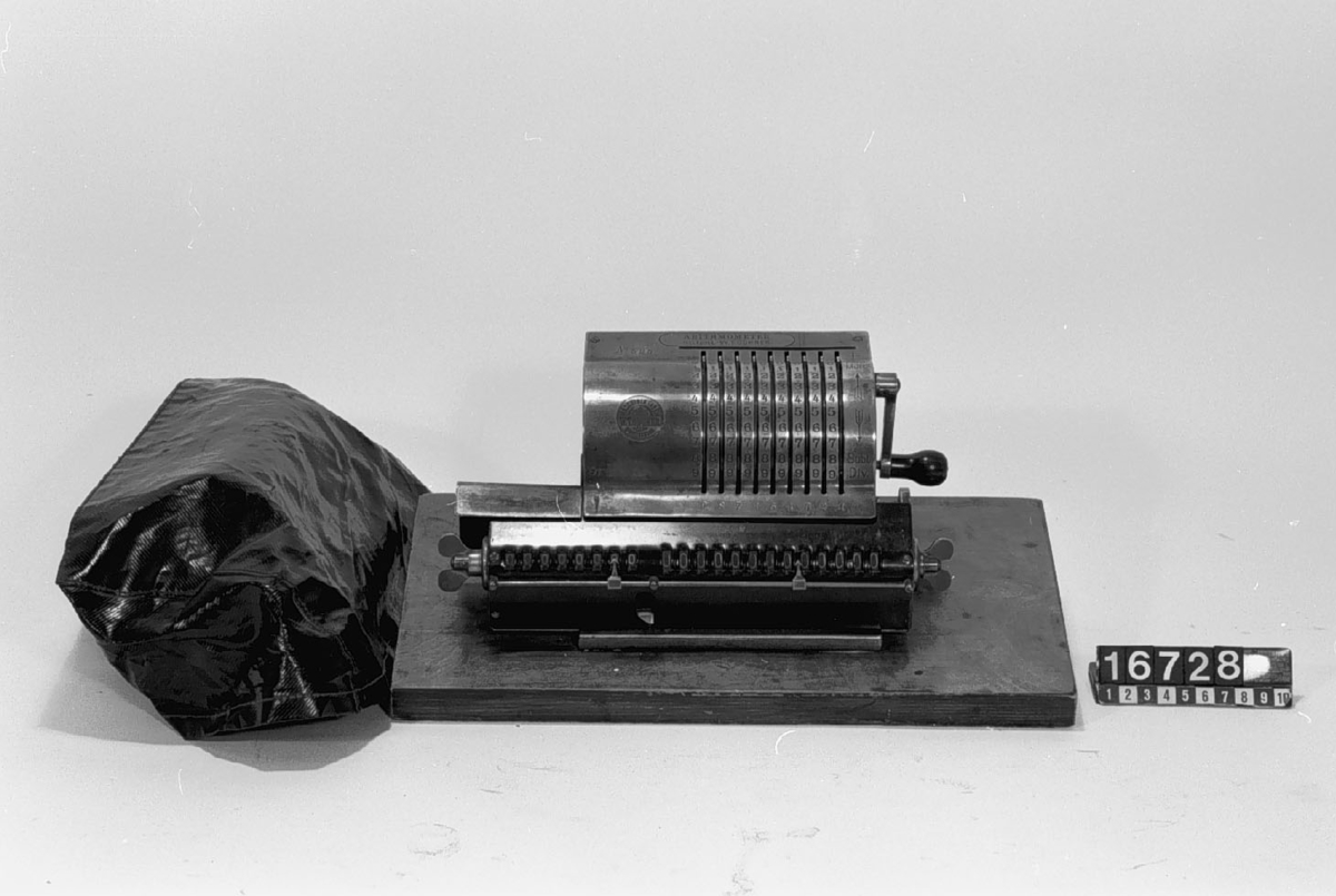 "Arithmometer" s.k. räknesnurra, monterad på träplatta. Höjd inklusive platta: 140 mm. "Maschinen Fabrik W.T. Odhner St. Petersburg".
Tillbehör: Tyghuv.