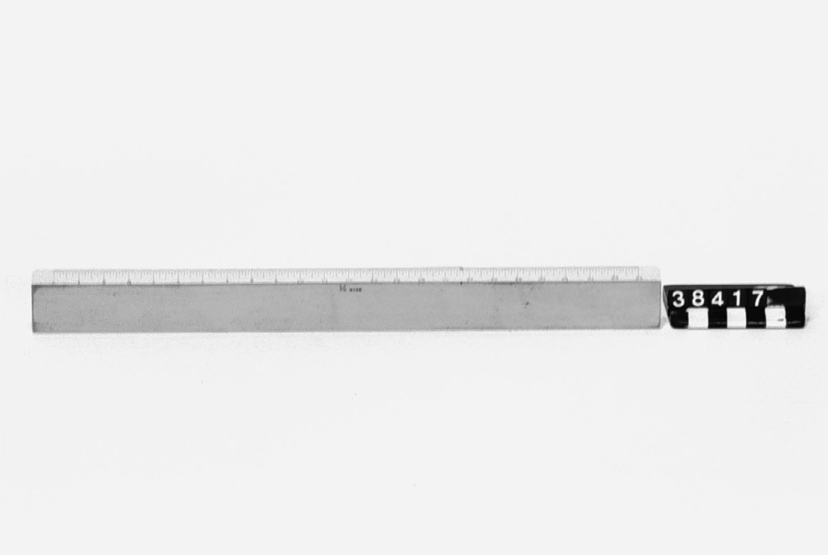 Linjal av polerat trä med vita skalor, delade i amerikanska tum. Skalorna märkta: "Full size" resp. "1/2 size". Märkning: POSTS ovanför en stiliserad örn. U.S. ST'D Linjalen har ägarbeteckningen "W.W." inristad.